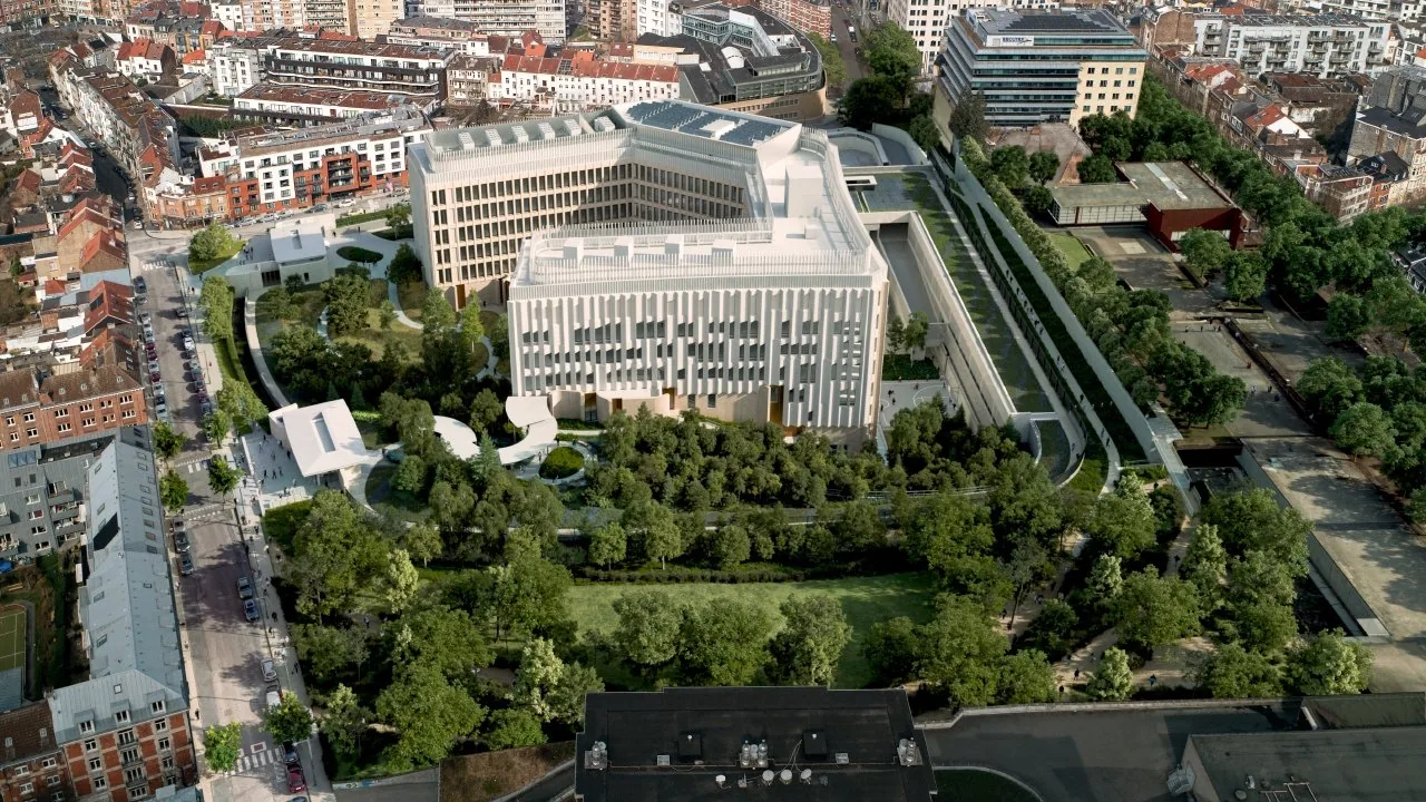 Une grande bâtisse moderne entourée d'espaces verts, d'arbres, et de bâtiments résidentiels dans une zone urbaine, vue aérienne.